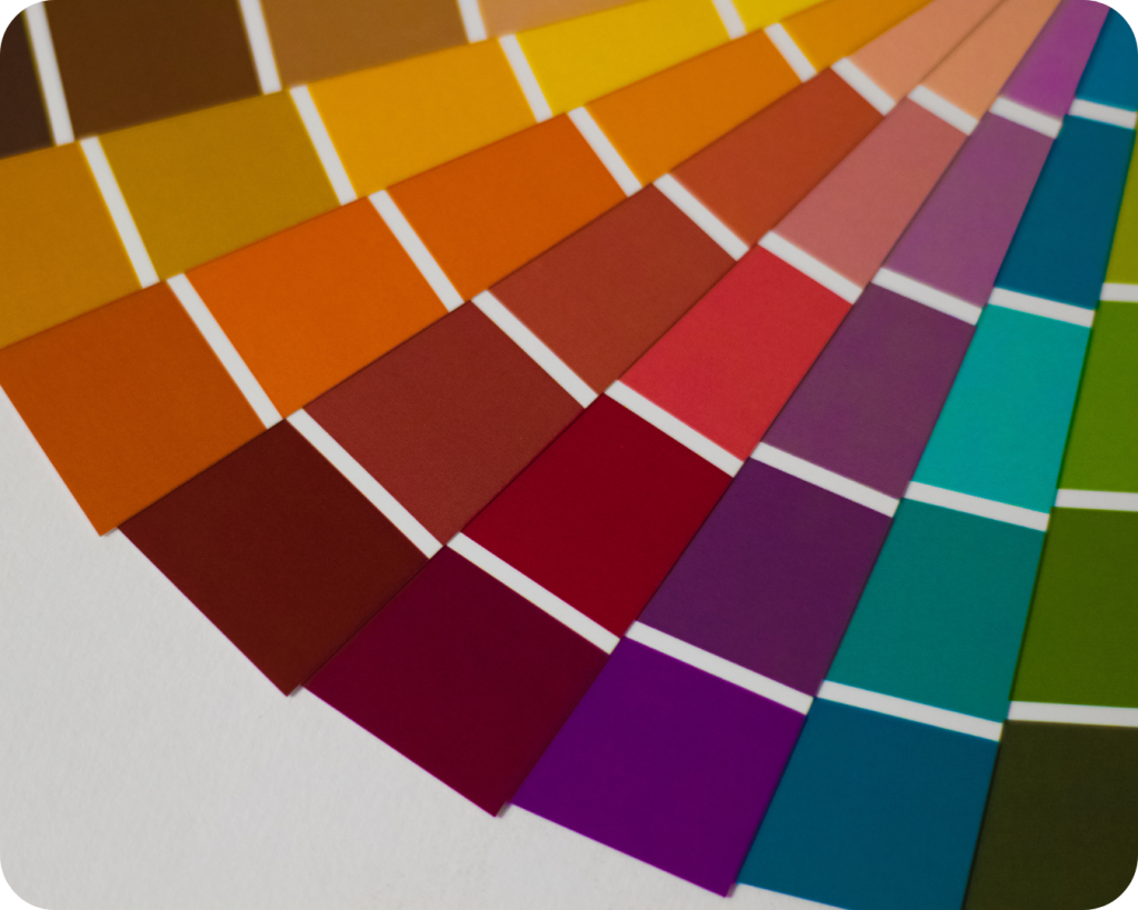 Uma paleta de cores em formato de leque, aberta e disposta sobre uma superfície branca. Ela exibe uma ampla gama de cores quentes e vibrantes, incluindo tons de marrom, laranja, vermelho, roxo, azul-petróleo e verde, perfeitos para inspirar projetos de verão.